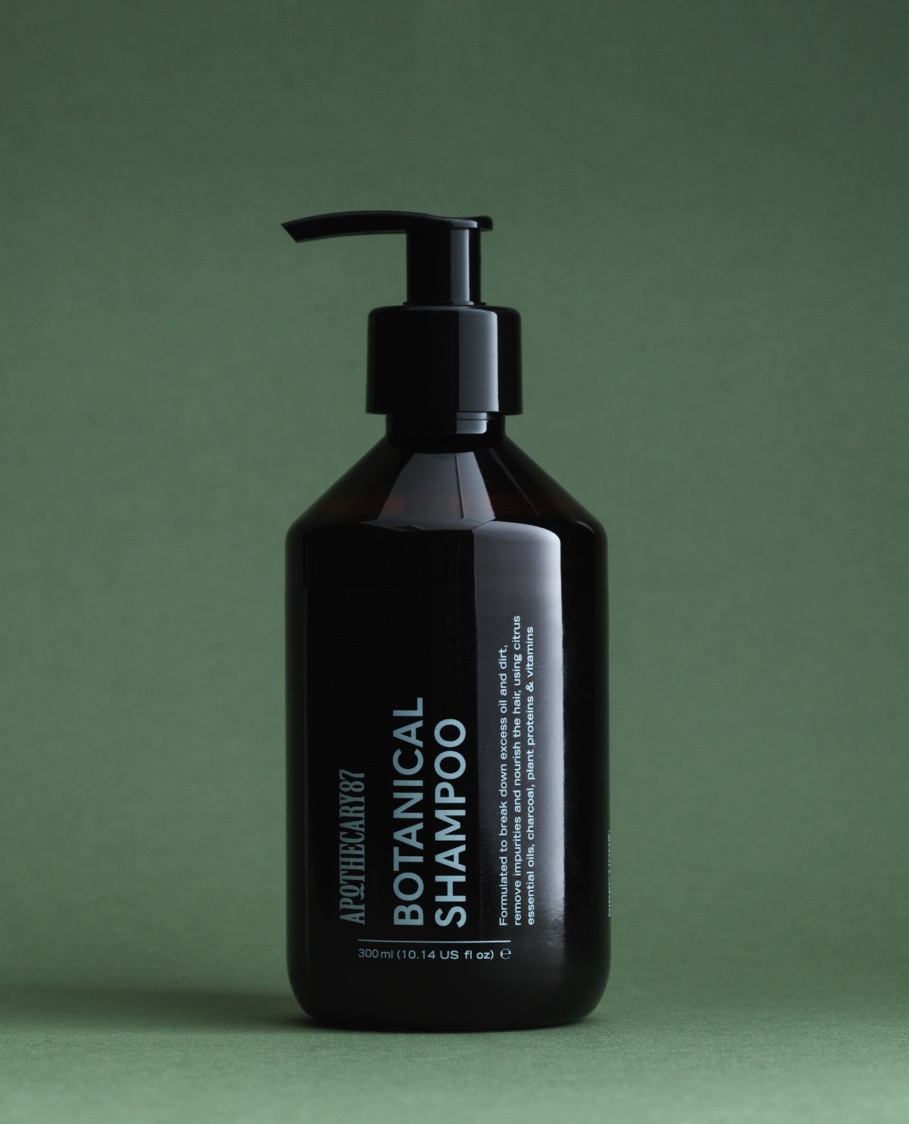 A brown bottle of Apothecary 87 Botanical Shampoo on a green studio background. Packaging design by 93ft.